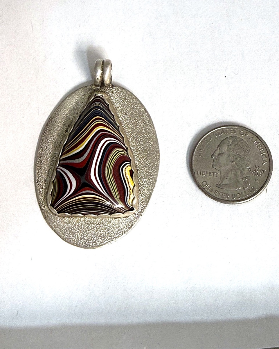 Sterling silver pendant set with an oval fordite cabochon showing banded layers of automotive paint.