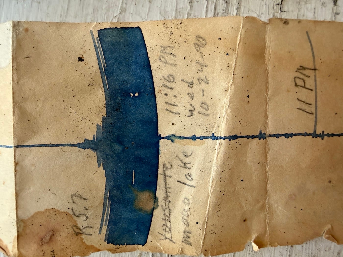 David Reynolds' paper seismograph tape recording the magnitude-5.7 Mono Lake earthquake of October 24, 1990 — a quiet blue trace, timing marks, and a heavy off-scale event blot, annotated by hand 'R=5.7 · Wed 10-24-90 · 11:16 PM · Yosemite / Mono lake.'