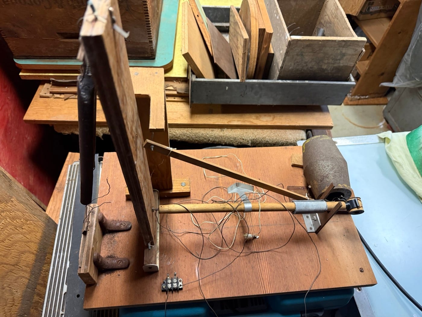 David Reynolds' complete hand-built horizontal-pendulum seismograph in the Soquel basement — the wooden frame and boom arm, the cylindrical magnet mass, the moving coil, and the fish-hook pivots.